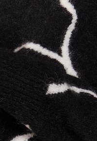 Tissu en laine noire avec un motif abstrait blanc. La texture semble douce et duveteuse, avec des fibres visibles créant une surface moelleuse.