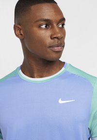 Camiseta deportiva de Nike con un cuerpo de color lila claro y hombros en verde menta, cuello redondo y tejido texturizado, con un logo blanco en el pecho.