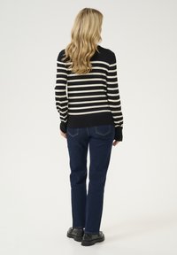 Juodas ir kreminis dryžuotas megztinis su priglundančiomis rankovėmis ir banguota apatine dalimi, derinamas su tamsiai mėlynomis tiesiomis kelnėmis ir juodais batais.