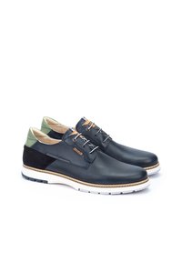 Chaussures en cuir perforé bleu marine avec accents verts et semelle en caoutchouc blanc. Présentent des coutures contrastantes et des œillets en métal pour les lacets.