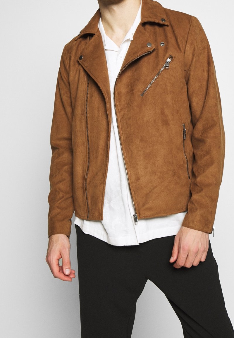 Brun faux suede motorcykeljakke med en struktureret krave, sølv lynlåse og sidelommer. Glat tekstur og tætsiddende design.