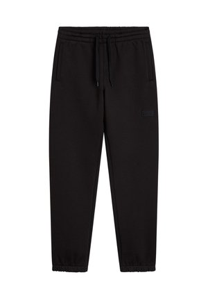 Person iført en hvid Vans Off The Wall t-shirt, sorte joggingbukser, sort sweatshirt bundet om livet og ternede slip-on sko.