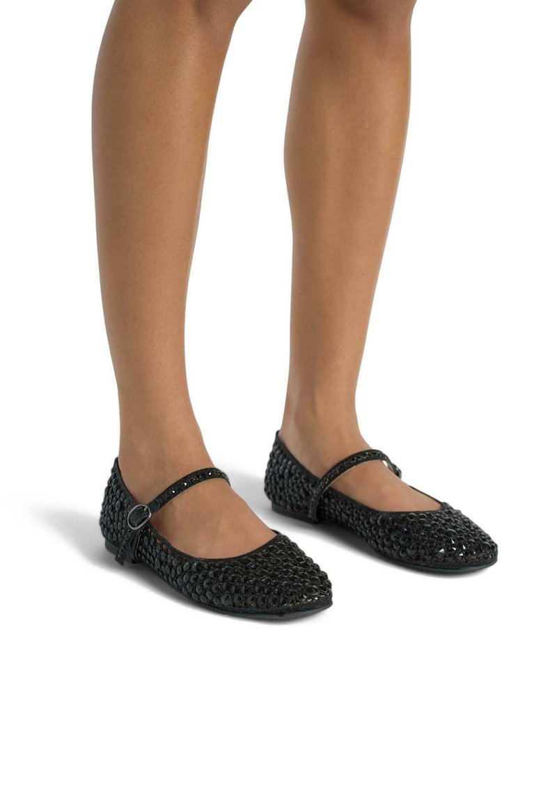 Ballerines noires avec une surface texturée, dotées d'une sangle sur le cou-de-pied et d'un bout arrondi. La chaussure comprend un détail en boucle métallique.