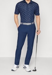 Námořnicky modrá polo košile s proužkovaným vzorem a krátkými rukávy, doplněná o tmavě modré kalhoty na míru a šedý pásek. Bílé sportovní boty s námořnicky modrými detaily.