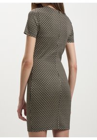 Robe à manches courtes avec une silhouette ajustée, motif géométrique noir et beige, et texture lisse. Longueur mi-cuisse avec un col arrondi.