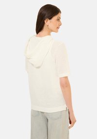 Haut blanc à manches courtes et à capuche avec un design texturé et perforé. Tissu semblable au coton ; coupe décontractée ; fentes sur les côtés au niveau de l'ourlet.