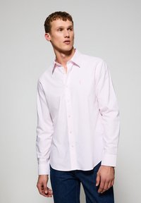 Lichtroze langarm shirt met witte strepen, knoopsluiting aan de voorkant, omgeslagen kraag en klein geborduurd logo op de borst.