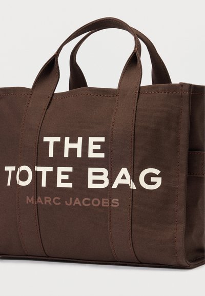 Καφέ τσαντάκι με διπλές λαβές, με την ένδειξη "Η ΤΣΑΝΤΑ" και "ΜΑΡΚ ΤΖΑΚΟΜΠ" τυπωμένες μπροστά με λευκά και καφέ γράμματα.