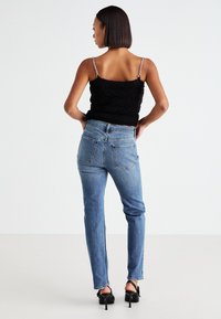 Black textured top with chain straps, high-waisted blue denim jeans, and black heeled sandals. Fitted silhouette with rear pockets.