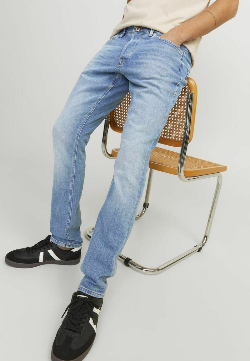 Helle blaue Jeans mit geradem Bein, im klassischen Fünf-Taschen-Stil und abgenutztem Look. Kombiniert mit schwarzen Sneakers.