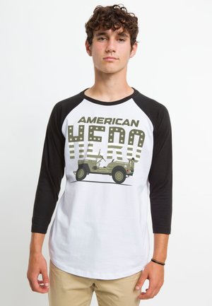 Hvid baseball-style T-shirt med sorte raglanærmer. Har teksten "AMERICAN HERO" og et grafisk billede af en grøn militær jeep med stjerner.