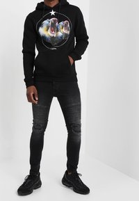 Haut à capuche noir avec une impression graphique d'animaux rugissants, associé à un jean skinny noir déchiré avec des accents en relief et des genoux déchirés. Baskets noires.