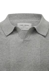 Graues Poloshirt mit Kragen und V-Ausschnitt. Hergestellt aus weichem Stoff, mit einem Etikett, das "CARL GROSS BLACK LINE" liest.