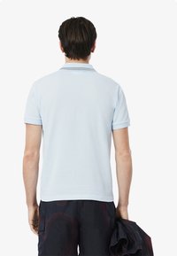 Ljusblå polo skjorta med en enfärgad design, korta ärmar, randig krage och en jämn, mjuk textur. Buren tillsammans med mörka cargoshorts.