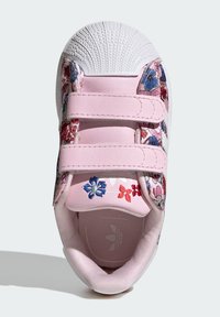 Roza superga s cvetličnim vezenjem, ima bel oklepni del na prstih, dva trakova z ježkom in teksturiran gumijast podplat. Vidna je mehka notranja podloga.