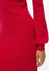 Abito rosso a maglia con texture a coste, maniche lunghe e silhouette attillata. La manica presenta un design leggermente a sbuffo.