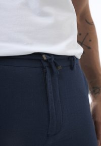 Navy blue pants with a textured fabric, featuring a zip closure and drawstring tie. Gold-colored hardware accents are visible.