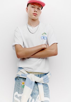 White t-shirt with a blue and green cup illustration, light blue striped sweater wrapped around a faded blue denim waistband.