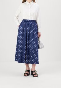 La skirt floral marin cu modele roz, talie elastică, lungime midi; asortată cu o cămașă albă cu nasturi și sandale negre cu toc.