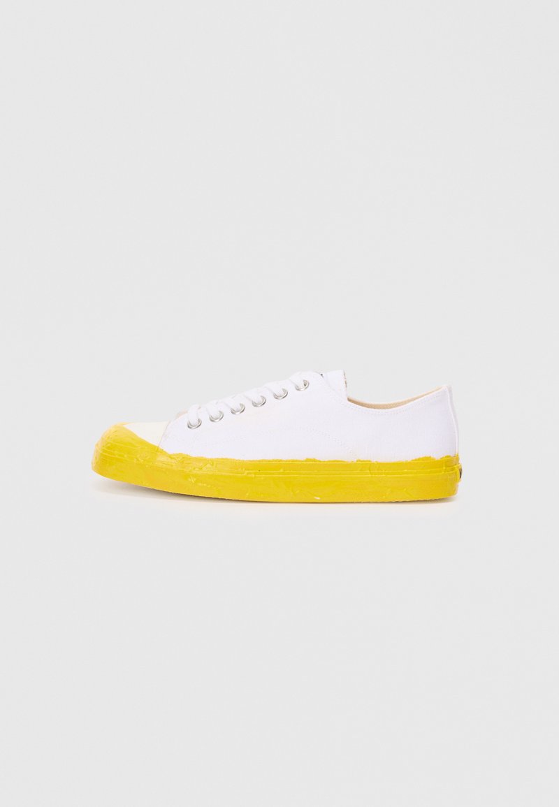 White canvas sneaker with a yellow rubber sole and toe cap. Features five metal eyelets for laces. Smooth texture with a structured design.