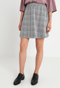Falda a cuadros gris con patrones negro y blanco. Corte en A, longitud a mitad de muslo, cinturilla elástica, combinada con zapatos negros con cordones.