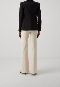 Czarna, dopasowana marynarka o gładkiej fakturze, zestawiona z kremowymi spodniami o rozkloszowanym kroju. Marynarka ma pojedynczy rozcięcie z tyłu i mankiety zapinane na guziki.