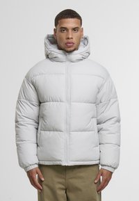 Pūkuotas pilkas pūkinis švarkas su aukštu apykakle ir pritvirtinta kapuce, su priekiniais užtrauktukais, elastinėmis rankovėmis ir išilginiu siuvimu.