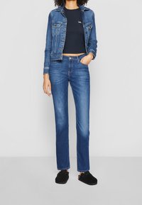Veste en denim et jeans bleu foncé. La veste comprend des boutons et des poches ; les jeans sont à coupe droite. Des chaussures noires à enfiler complètent la tenue.