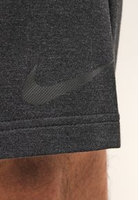 Pantalones cortos deportivos de color gris oscuro, hechos de una tela texturizada, con un logo negro de Nike en el lado izquierdo, con un dobladillo plano y costuras cuidadas.