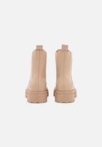 Botas de tobillo de cuero beige con paneles laterales elásticos, puntera redonda y suelas de goma gruesa. Cuenta con asas en la parte trasera para un fácil calzado.