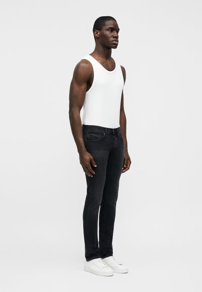 Λευκό αμάνικο τοπ συνδυασμένο με στενά μαύρα τζιν και λευκά αθλητικά παπούτσια, που παρουσιάζει ένα απλό, μοντέρνο σχέδιο και εφαρμοστή σιλουέτα.