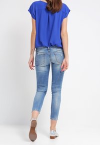 Modrá blůza, světle modré džíny, délka po kotníky. Textura džínů vykazuje detail žíhání. Stříbrné boty s nízkým podpatkem.