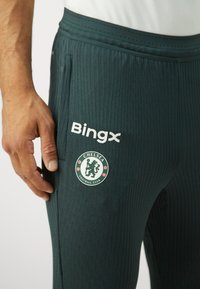 Pantalons de sport verts avec un design texturé, une taille élastique, le logo de Chelsea Football Club et la marque "Bingx".