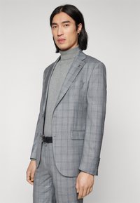 Completo grigio a quadri con giacca aderente, pantaloni abbinati e dolcevita grigio chiaro. Presenta un sottile logo in evidenza sul risvolto.