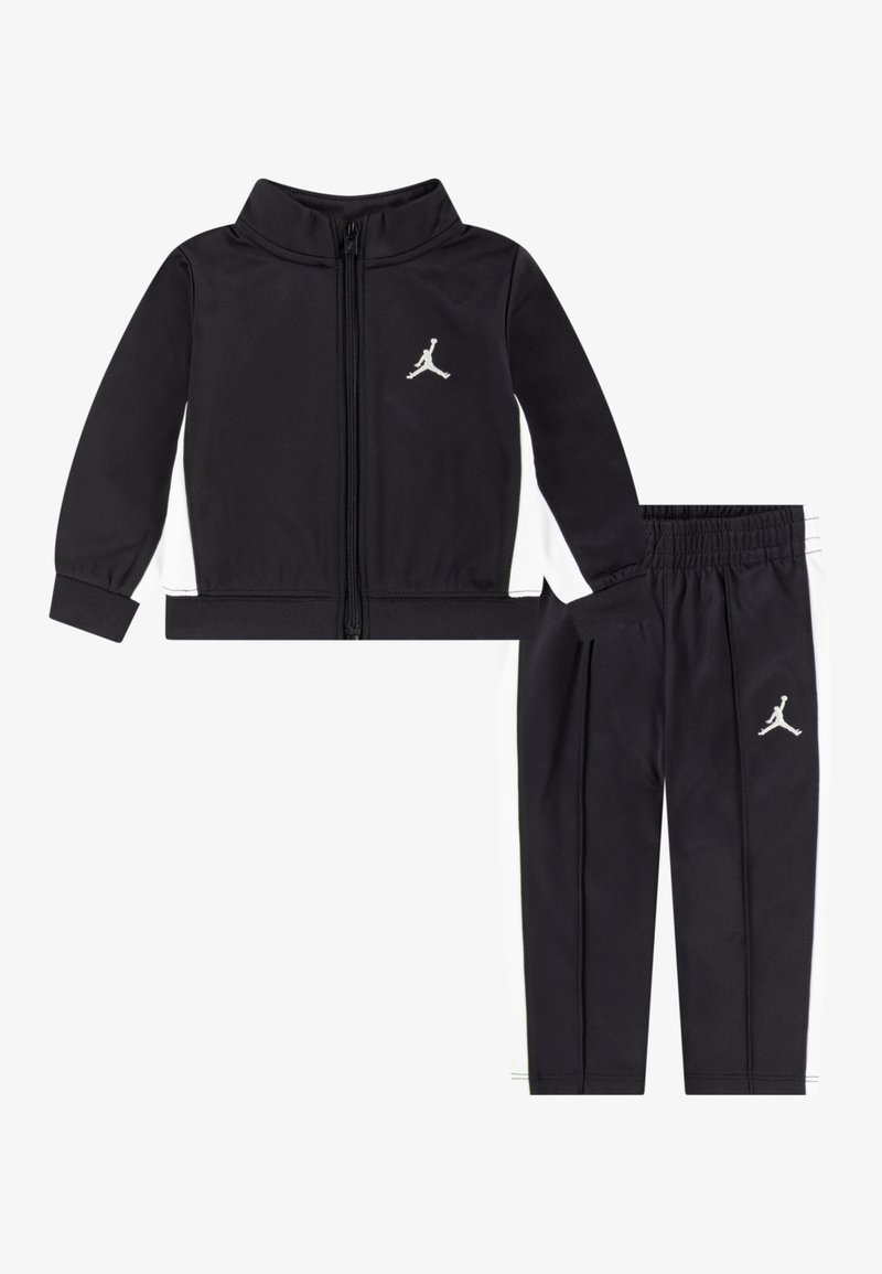 Schwarze Zip-Up-Jacke und passende Hose, beide aus glattem Stoff. Die Jacke hat weiße Seitenpaneele und ein silbernes Jordan-Logo; die Hose hat einen elastischen Bund.