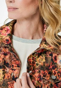 Jeansjack met bloemenpatroon in oranje, roze en groene tinten. Voorzien van drukknoopsluiting en een contrasterend kraagontwerp.