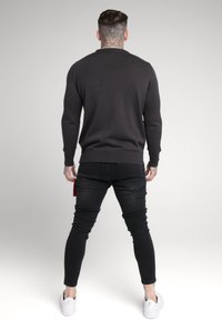 Mörkgrå tröja med ribbad struktur, åtsittande ärmar och rundad halsringning. I kombination med svarta tajta jeans och vita sneakers.