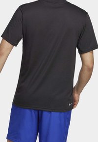 Man wearing plain black short-sleeve t-shirt and bright blue shorts, shown from the back against a plain background.