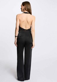 Combinaison noire sans dos avec un col halter, un design à jambes larges, une texture lisse et de légers poches à l'arrière.