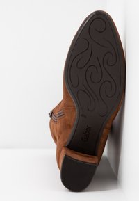Bottine en daim marron avec semelle en caoutchouc noire à motif et talon bas, semelle visible vers le haut affichant la marque Gabor et la taille 4½.