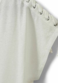 Gros plan sur un tissu blanc avec des œillets métalliques et des lacets blancs passés pour un détail de fermeture réglable.