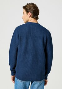 Granatowy sweter z dzianiny o fakturowanym wzorze, z prążkowanymi mankietami i dołem. Posiada subtelny dekolt oraz luźny krój dla wygody.
