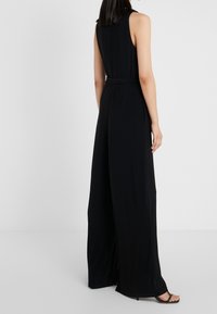 Mono negro sin mangas con un ajuste relajado, cintura ceñida, piernas amplias y una tela suave. Presenta un diseño limpio y minimalista.