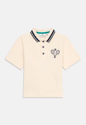 Krēmkrāsas īsroku polo krekls ar jūras zilām svītrām apkaklē, trim jūras ziliem pogām un krustotu tenisa raketiņu izšuvumu uz kreisās krūtis.