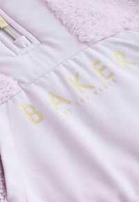 Svetloružová bunda s plyšovými kožušinovými akcentmi, s výrazným zlatým logom "BAKER by TED BAKER" na prednej strane.