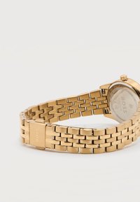 Ρολόι μπρασελέ με συνδέσμους από χρυσό μέταλλο με κούμπωμα χαραγμένο "BOSS", που δείχνει την πίσω πλευρά του καντράν με ορατή την μάρκα και τις σημάνσεις.