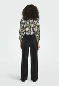 Gėlėtais raštais dekoruota palaidinė su pūstomis rankovėmis žalia, geltona ir purpurine spalvomis, derinama su juodomis plisė platėjosiomis kelnėmis. Lygus tekstūra, laisvas siluetas.