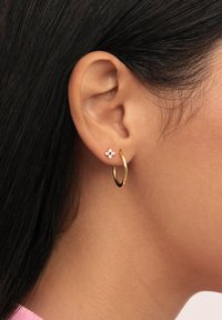 Pendiente de aro de oro combinado con un pequeño pasador floral; el aro es brillante con una superficie lisa, mientras que el pasador presenta un diseño de flor rosa con acentos blancos.