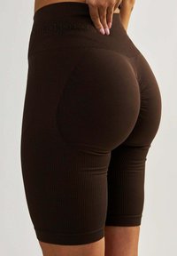 Brązowe rowerki z prążkowanego materiału z wysokim stanem, na którym wyciśnięte jest słowo "kształt". Gładka tekstura, dopasowany krój podkreślający krągłości.