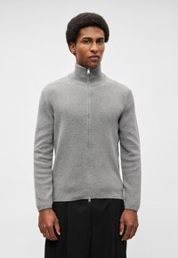 Γκρι φούτερ με φερμουάρ, φτιαγμένο από μαλακό πλεκτό ύφασμα, με ψηλό γιακά και μακριά μανίκια, διαθέτοντας μια διακριτική ριμπ ύφανση και ασημένιο φερμουάρ.